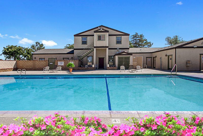 Pool with Clubhouse, chairs, and pink flowers